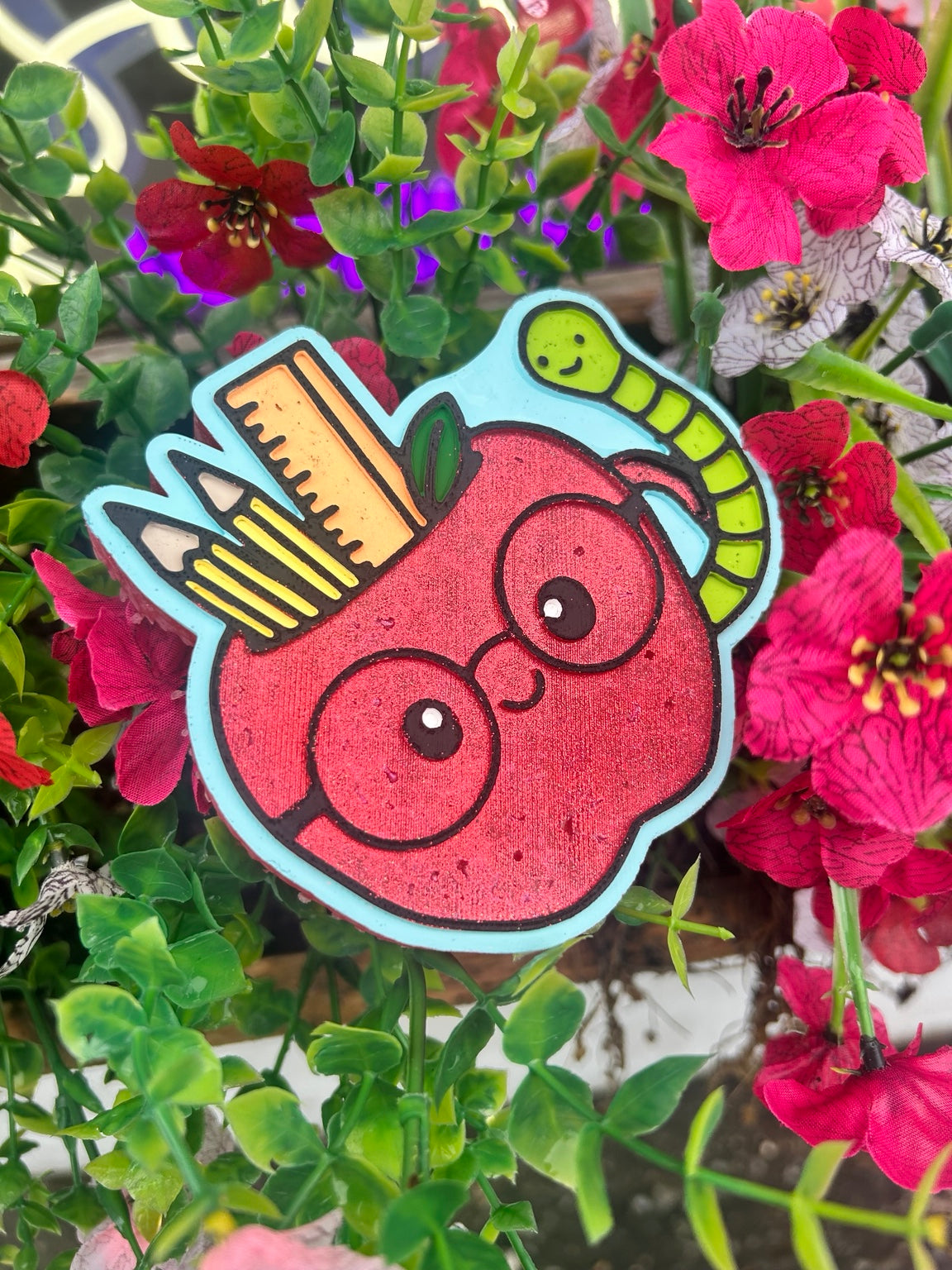 Teacher apple car freshie with glasses, two pencils, an orange ruler and a smiling green worm, painted red with a light blue outline