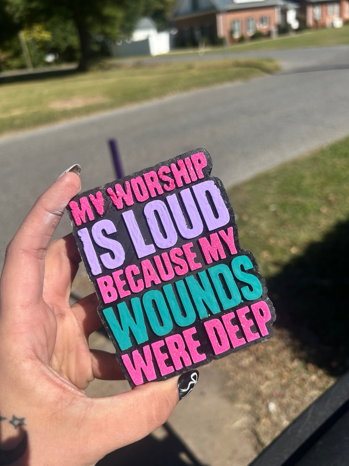 My Worship Is Loud Because My Wounds Were Deep car freshie, pictured with bright pink, lavender and teal lettering on a black background